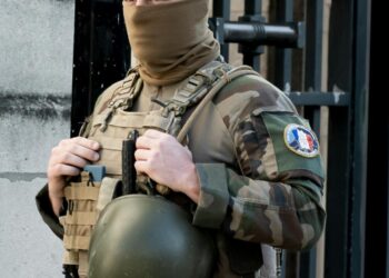 A U.S. soldier is handcuffed outside a military building, surrounded by police.