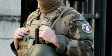 A U.S. soldier is handcuffed outside a military building, surrounded by police.