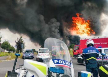 Flames engulf a luxury home, police cars surrounding the scene after a firebomb attack.