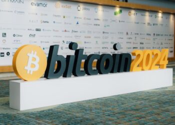 J. Christopher Giancarlo speaking at a finance conference with blockchain visuals in background.