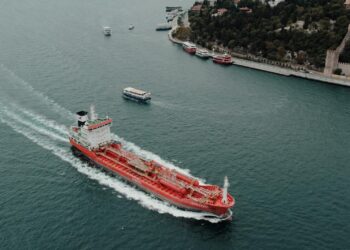 An oil tanker navigating the Strait, overlaid with Bitcoin and financial symbols.