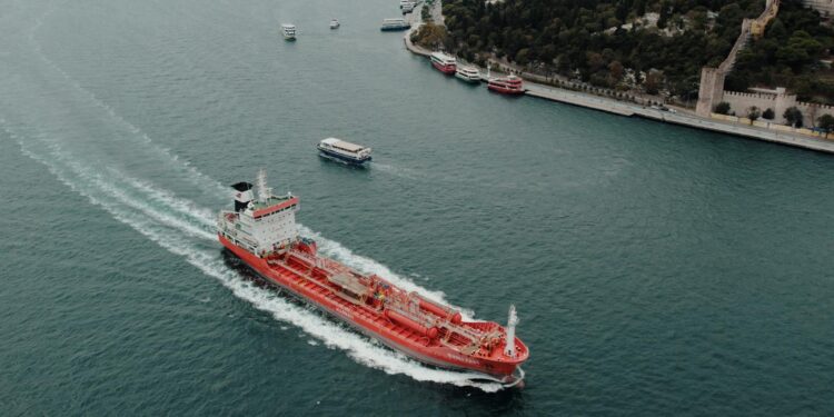 An oil tanker navigating the Strait, overlaid with Bitcoin and financial symbols.