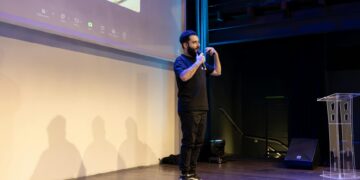 Sam Bankman-Fried speaking at a conference with FTX branding in the background.