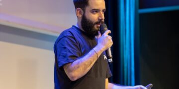 Dan Finlay speaking at a crypto conference, gesturing passionately to the audience.