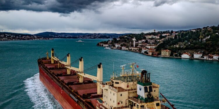 A cargo ship navigating the Strait of Hormuz with a shipping route map overlay.