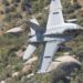 F-15E aircraft in flight over rugged terrain, with smoke rising from a distant location.