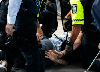 Benjamin Pasternak in handcuffs being led away by police officers at a courthouse.