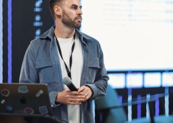 Justin Sun speaking at a cryptocurrency conference, with attendees and media in the background.