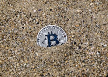 A stranded ship in the Strait of Hormuz with digital currency symbols overlayed.