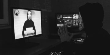 A hacker sitting at a computer with crypto-related graphics on the screen.