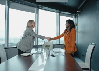 Payward CEO shaking hands with Bitnomial executives in a modern office setting.