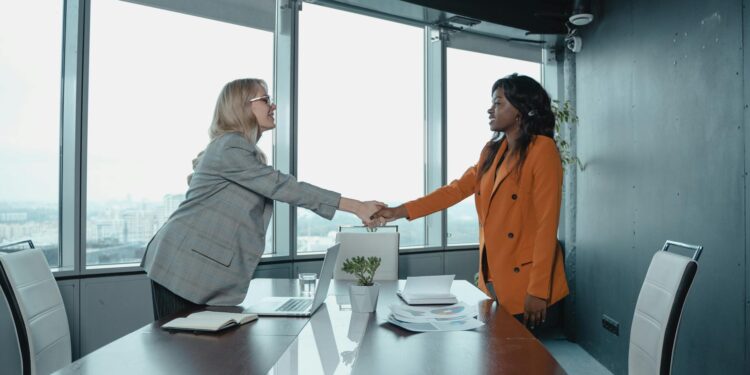 Payward CEO shaking hands with Bitnomial executives in a modern office setting.