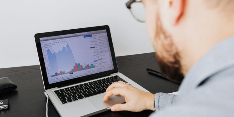 A person analyzing cryptocurrency data on a laptop screen with charts and graphs displayed.
