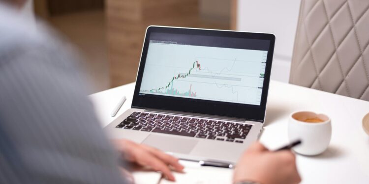 A person examines cryptocurrency charts on a computer screen in a modern office.
