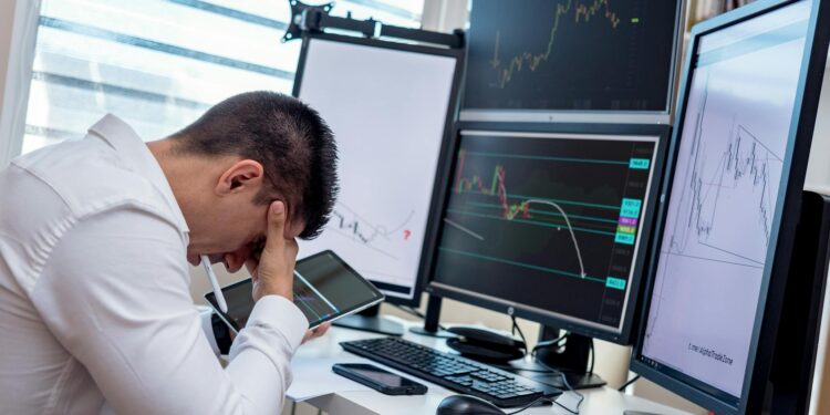 Falling stock charts and a worried trader at a financial market desk during tense economic times.