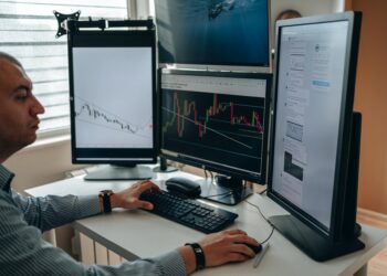 A programmer working at a computer, surrounded by charts and financial data.