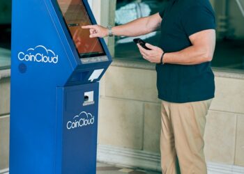 A crypto ATM in a public space with a warning sign about fraud risks.