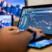 US soldier in military uniform at a desk with a laptop and crypto trading charts.