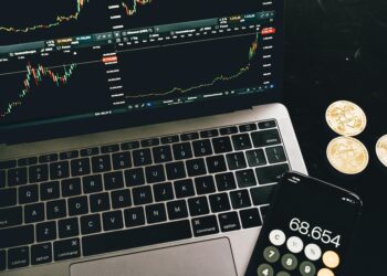 Bitcoin coins arranged beside a calculator and financial graphs, symbolizing ETF investments.