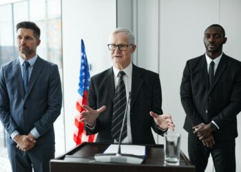 John Ternus smiling at a press conference, joined by Tim Cook, announcing leadership changes.