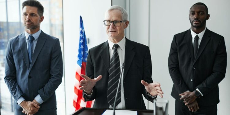 John Ternus smiling at a press conference, joined by Tim Cook, announcing leadership changes.