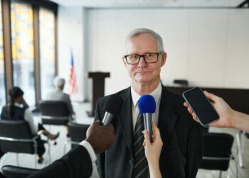 Eric Swalwell speaking at a press conference, with reporters and cameras in attendance.