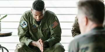 Uniformed soldier in handcuffs at a military base, reflecting insider trading concerns.