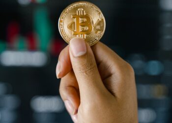 Person holding a Bitcoin Visa card amid cryptocurrency symbols and financial charts.