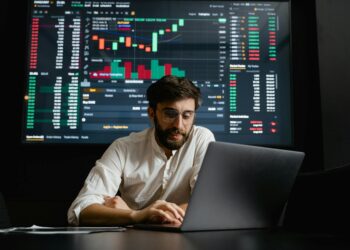 Crypto trader analyzing charts on a laptop, with oil barrel and dollar signs in the background.