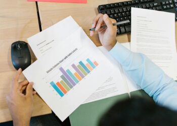 A financial analyst reviewing charts with Bitcoin symbols and ETF documents on a desk.