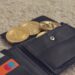A digital illustration of a cracked cryptocurrency wallet with coins spilling out.