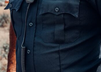 An ICE agent in uniform stands outside a building during a law enforcement operation.