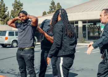 Police arresting a cryptocurrency founder outside a corporate building amidst news coverage.