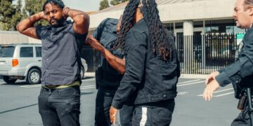 Police arresting a cryptocurrency founder outside a corporate building amidst news coverage.