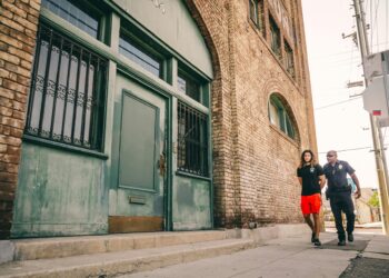 Huione Group Chairman in handcuffs, escorted by officers, in front of a court building.