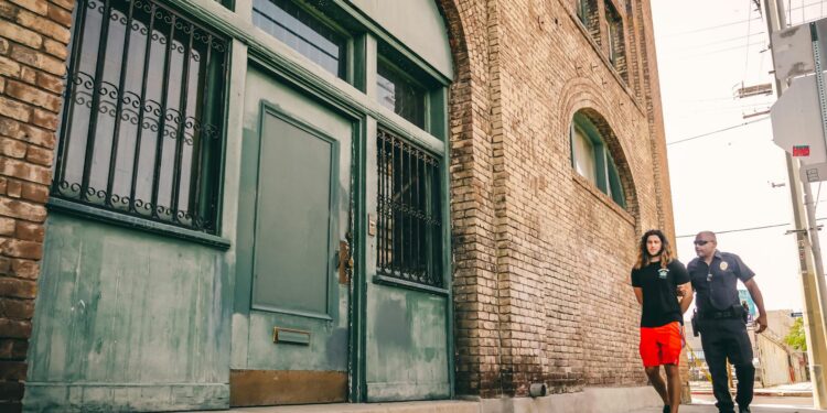 Huione Group Chairman in handcuffs, escorted by officers, in front of a court building.