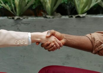 Two business professionals shake hands over a smartphone, symbolizing a strategic acquisition.