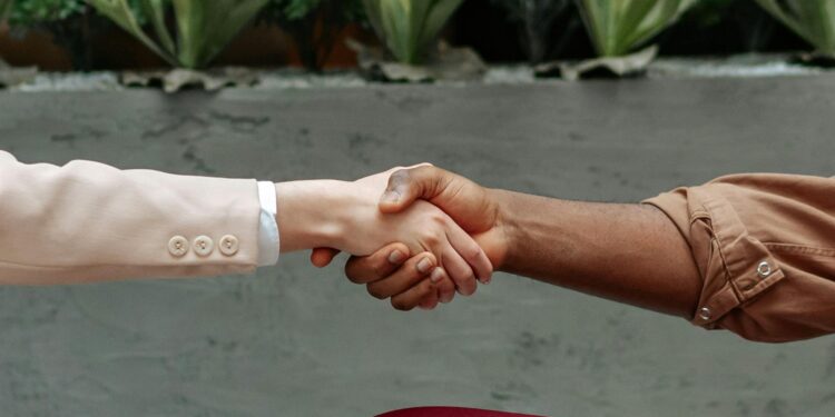 Two business professionals shake hands over a smartphone, symbolizing a strategic acquisition.