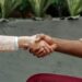 Two business professionals shake hands over a smartphone, symbolizing a strategic acquisition.