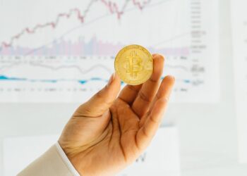 Brett Redfearn smiling, standing in an office with financial charts and crypto assets in background.