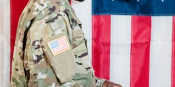 US soldier in military uniform with financial charts and Polymarket logo in the background.