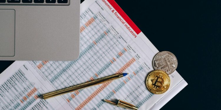 A Bitcoin coin alongside financial documents and a regulatory book on a desk.