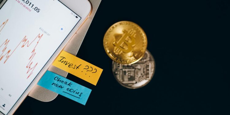 A person checks cryptocurrency prices on a smartphone with financial documents beside it.