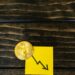 Stacks of cryptocurrency tokens with a downward arrow, symbolizing market decline.