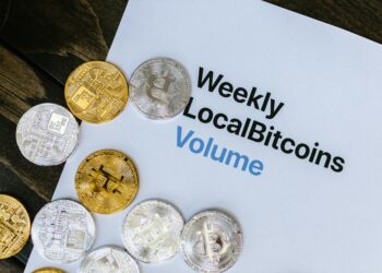 A close-up of Bitcoin tokens stacked on financial documents and a calculator.