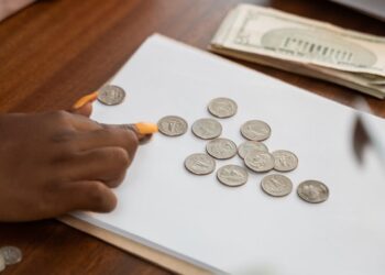 Hands counting cryptocurrency coins with a financial document and calculator in the background.