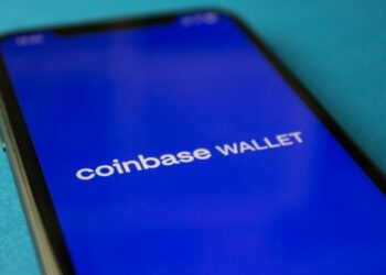 A person using a smartphone displays the Coinbase app with crypto loan options visible.