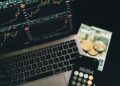 A laptop displaying blockchain graphics alongside cryptocurrency coins and financial charts.