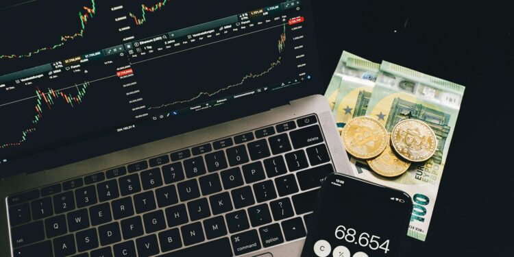 A laptop displaying blockchain graphics alongside cryptocurrency coins and financial charts.