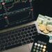 A laptop displaying blockchain graphics alongside cryptocurrency coins and financial charts.